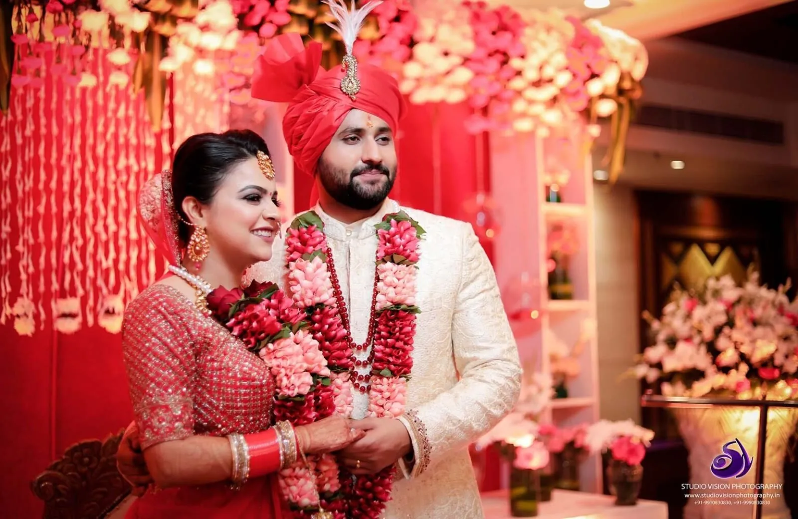 Bride and groom garlanded under a floral mandap
